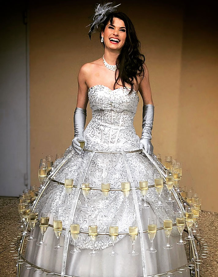Porteuse de champagne en robe cocktail grise à paillettes argentées tenant un plateau de flûtes